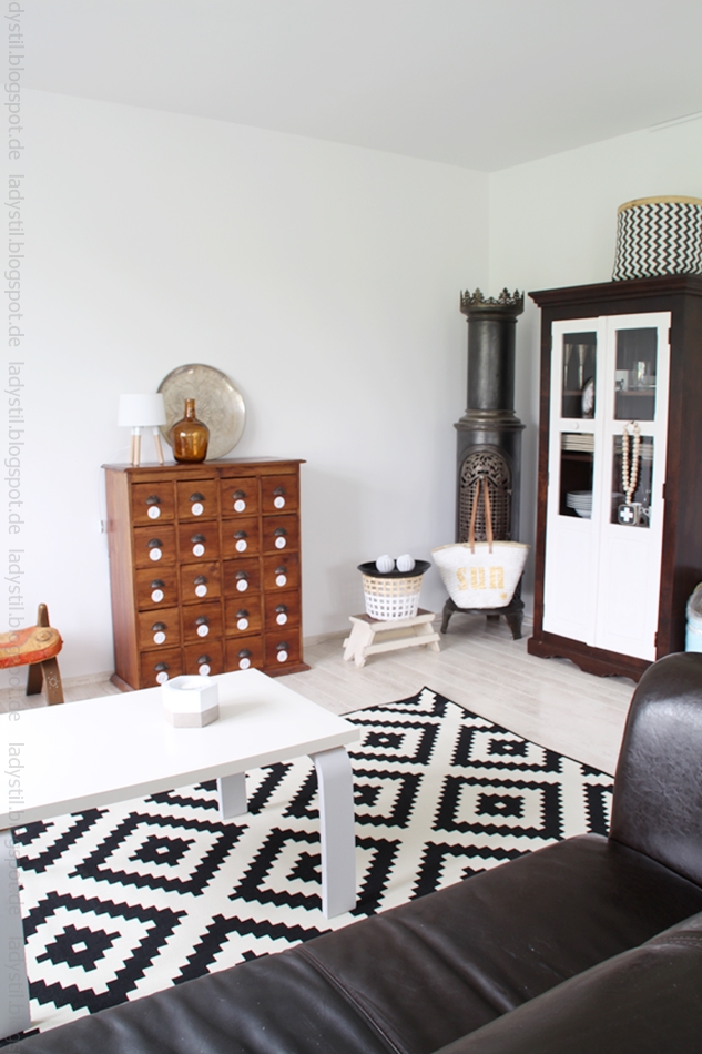 Wohnzimmeransicht mit Vitrine mit weißen Türen, schwarzweißem Teppich und antikem Apothekerschrank