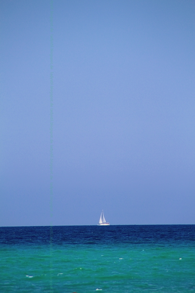 Blick übers türkisfarbene Meer mit weißem Segelboot und strahlendblauem Himmel