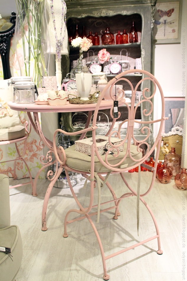 verschnörkelter Eisenstuhl in rosa vor einem runden Tisch mit Deko
