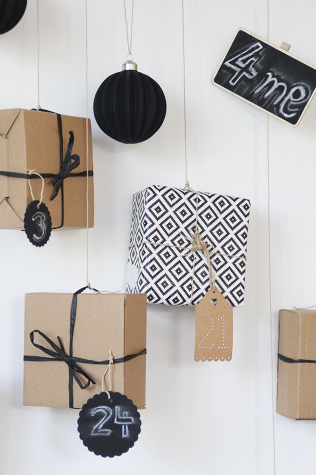Adventkalender Geschenke in Packpapier und schwarzweißem Papier hängen an einem Ast