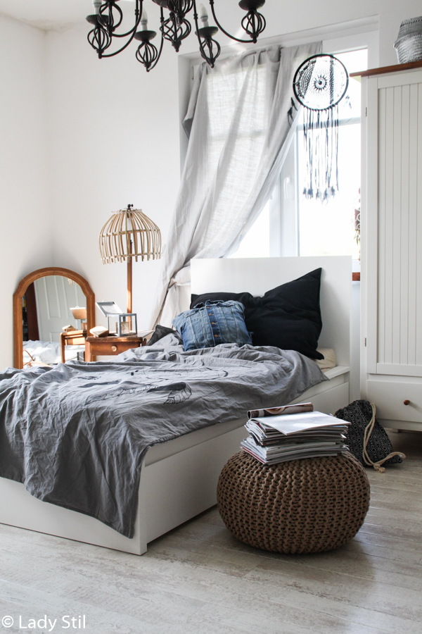 Schlafzimmer mit weißen Möbeln und grauer Bettwäsche mit Traumfänger Motiv sowie Holzspiegel im Boho Look